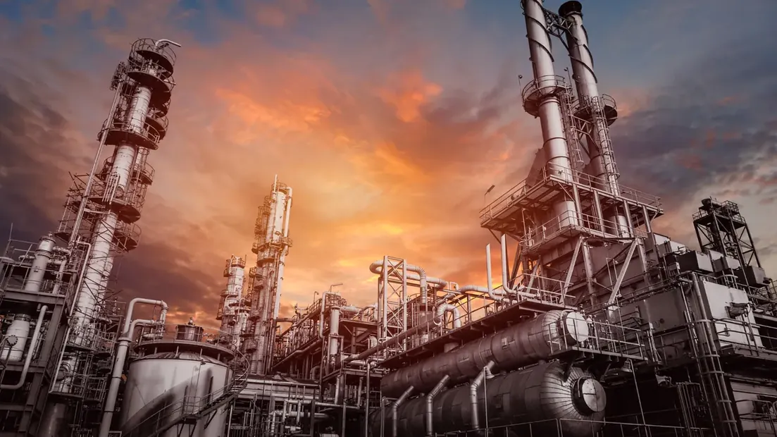 Refinaria iluminada ao entardecer com torres e tubulações